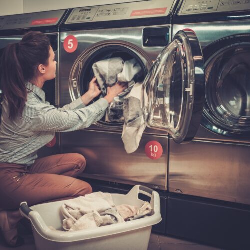 Beautiful woman doing laundry at laundromat shop.